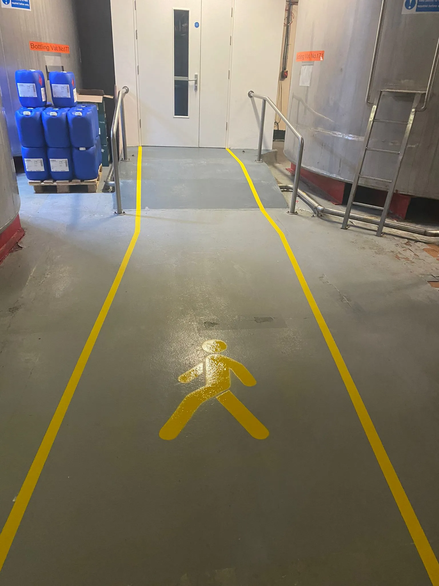 Yellow pedestrian walkway markings guiding safe movement through a distillery warehouse