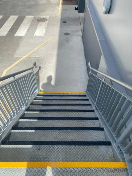 Black anti-slip step nosings and yellow UV line marking leading from warehouse stairs to pedestrian route
