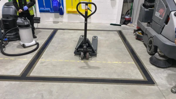 Black and gold bordered pallet truck storage bay marked on a warehouse floor with UV line marking