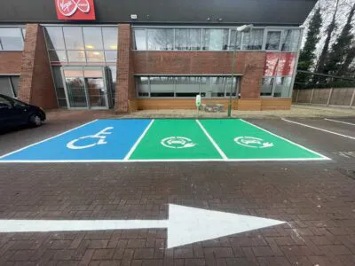 Blue accessible parking bay and green EV charging bays with directional road arrow