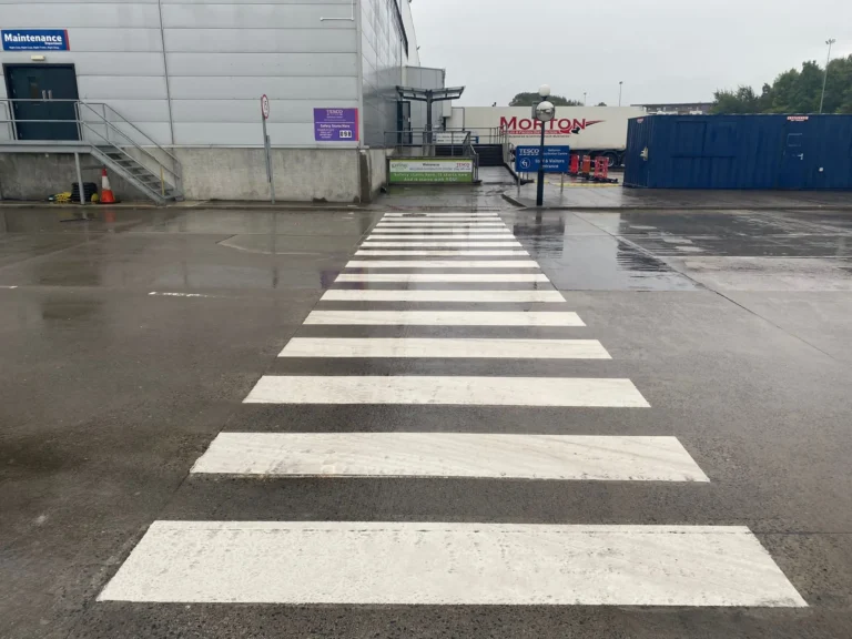 White pedestrian crossing line marking across an industrial access road