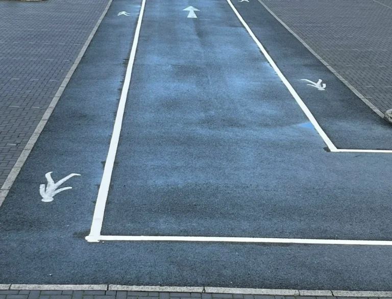 White pedestrian walkway line marking with directional arrows in a car park