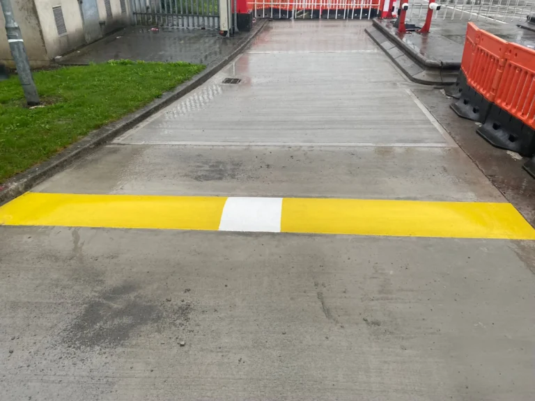 Yellow and white safety road marking across an industrial access route
